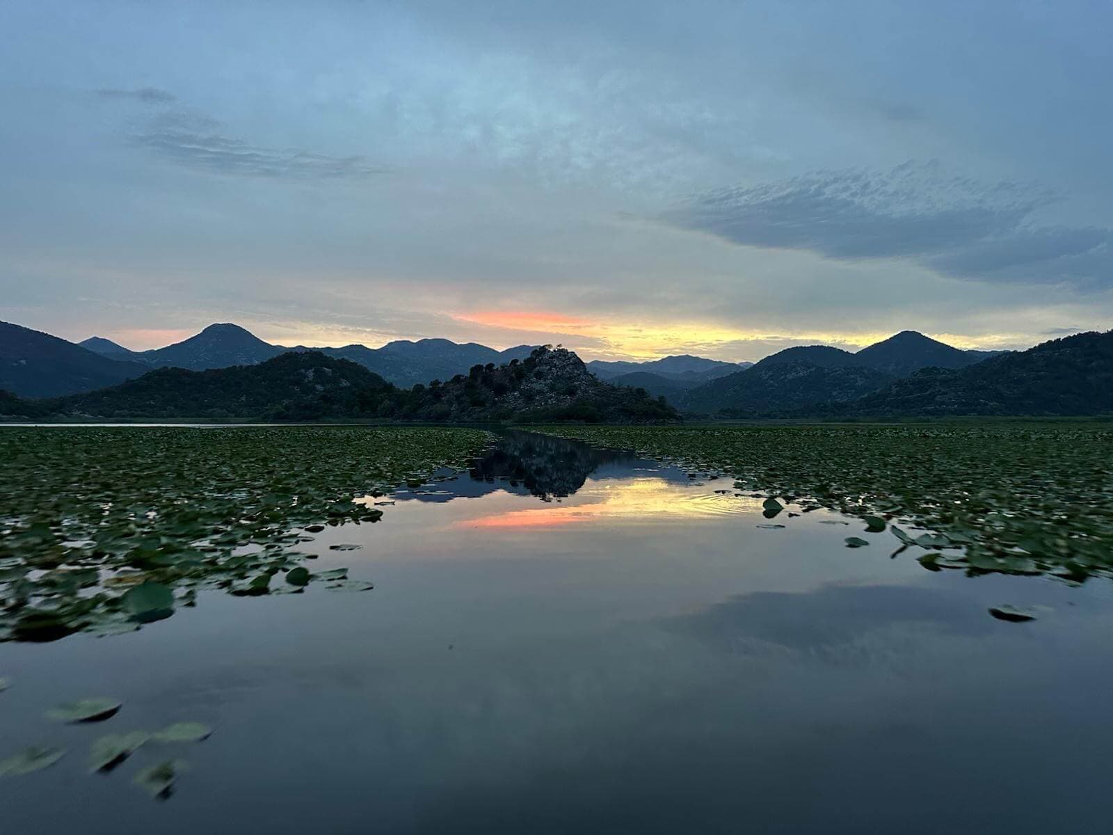 Berge, die sich bei Sonnenuntergang im stillen Wasser des Skadar Sees spiegeln
